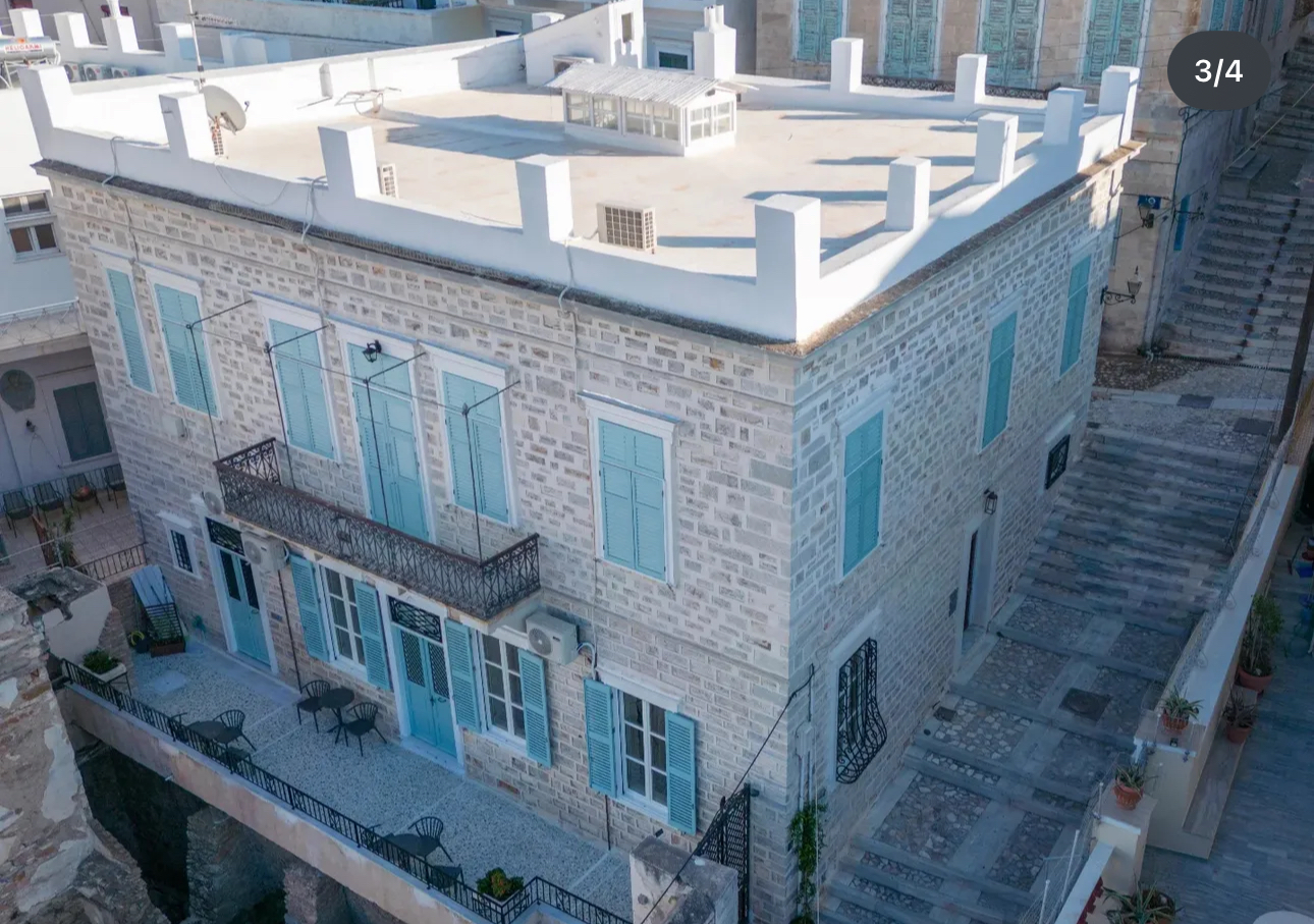 The stone facade of the Syra di Giovanni 1862 mansion with light blue shutters in Ermoupoli, Syros